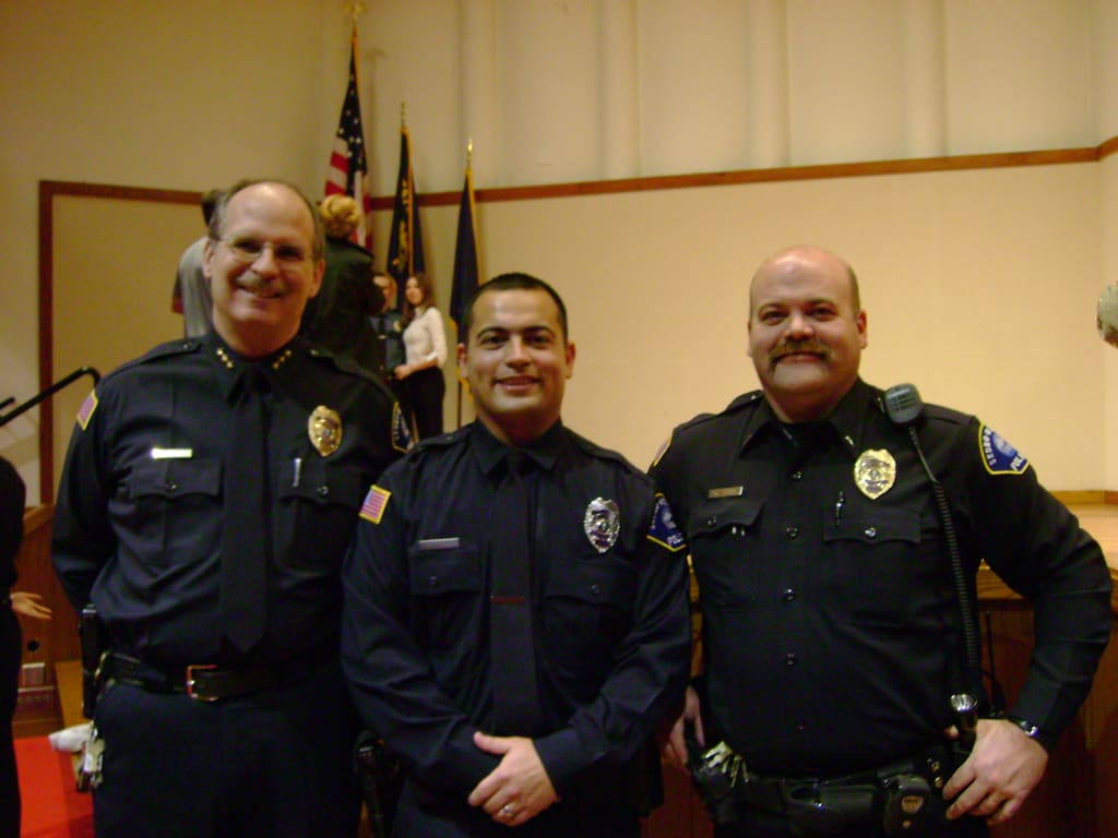 Adam Musgrove in his early law enforcement uniform, smiling with two fellow officers during a graduation ceremony.